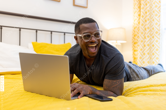 Black man working from home on laptop in bed