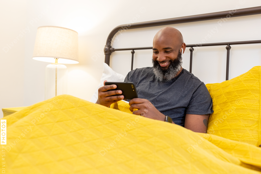 Black man with gray beard on phone in bed at home
