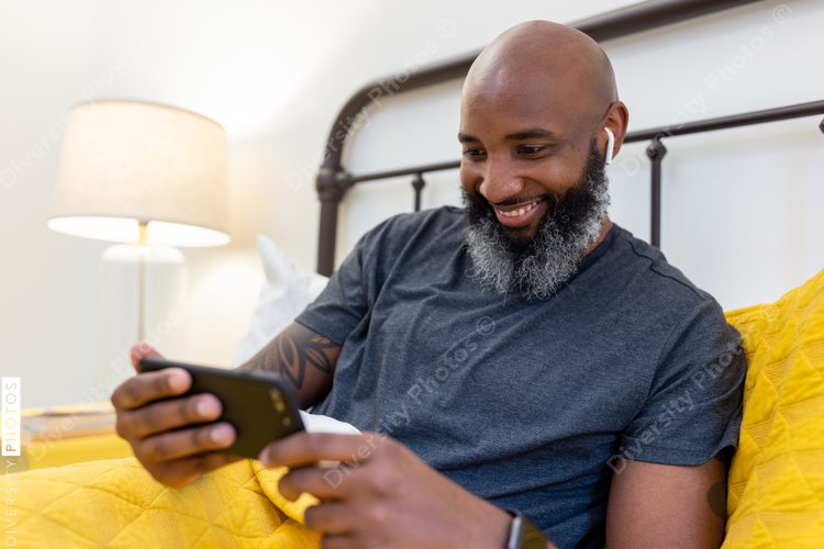 Black man with gray beard on phone in bed at home
