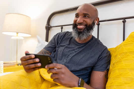 Black man with gray beard on phone in bed at home