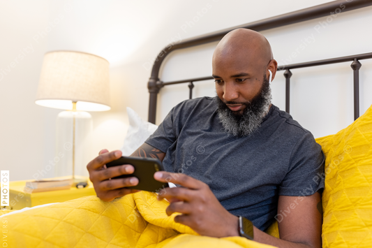 Black man with gray beard on phone in bed at home