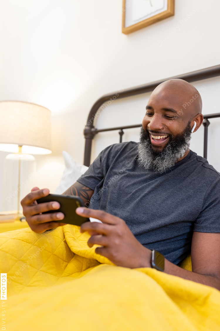 Black man with gray beard on phone in bed at home