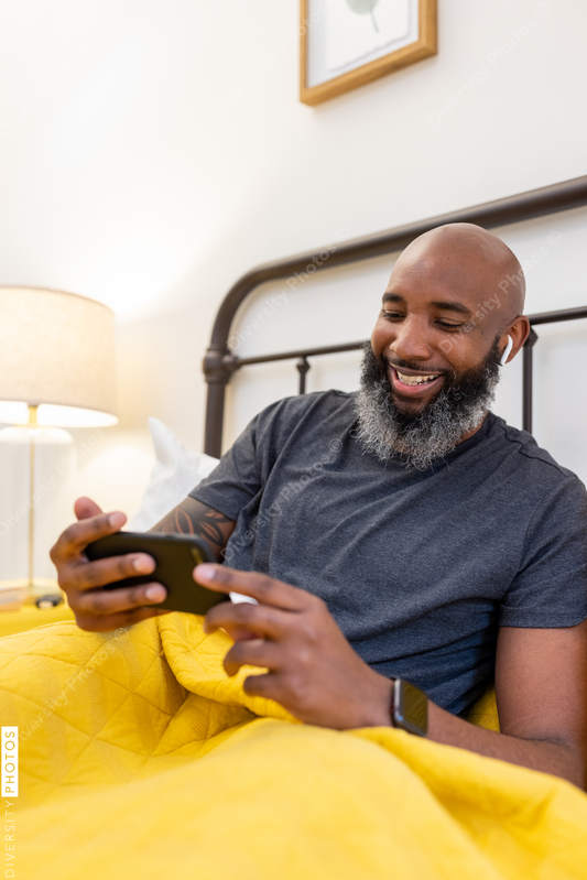 Black man with gray beard on phone in bed at home