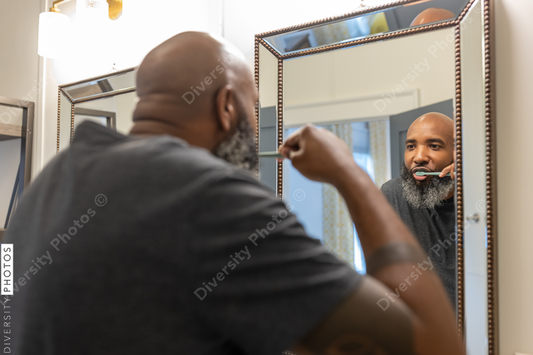 Black man with gray beard brushes teeth in bathroom at home