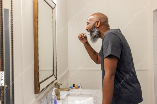 Black man with gray beard brushes teeth in bathroom at home