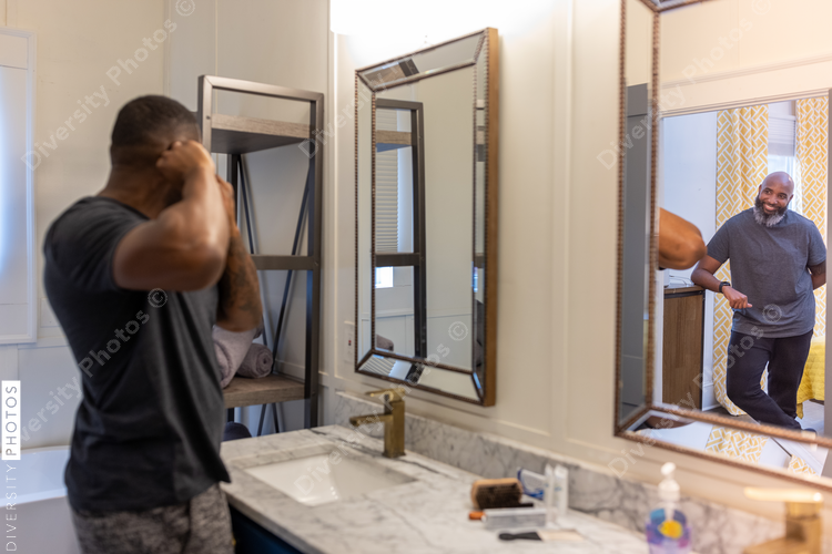 Black man puts earrings in ear, looking in mirror in bathroom, grooming