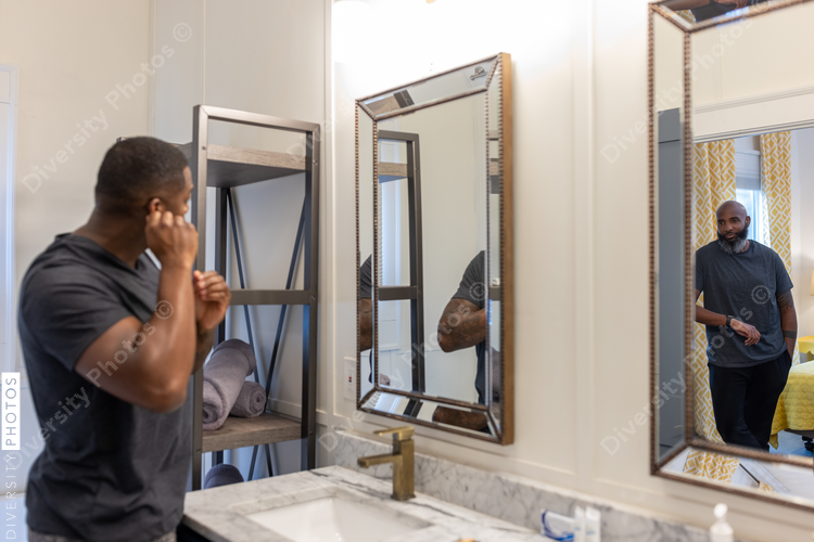 Black man puts earrings in ear, looking in mirror in bathroom, grooming