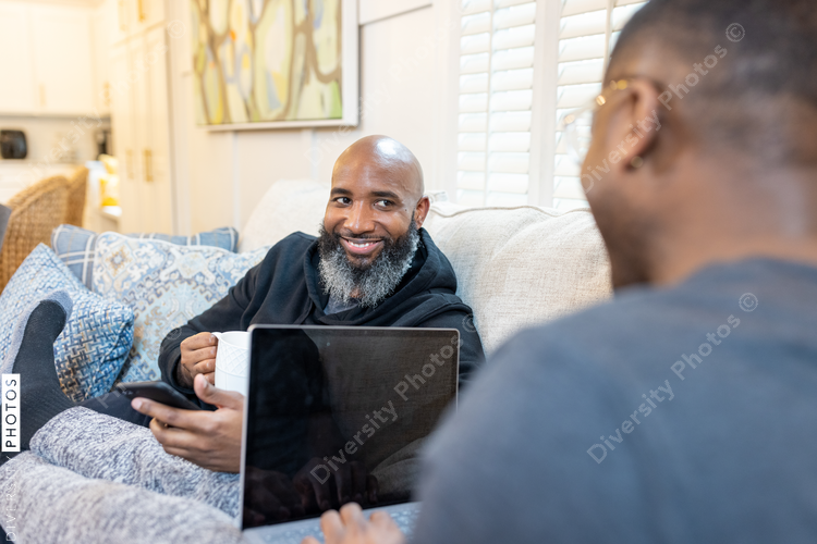 Black gay men have conversations on couch at home