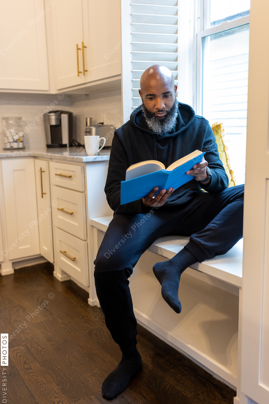 Black man, cozy, reading book in nook at home