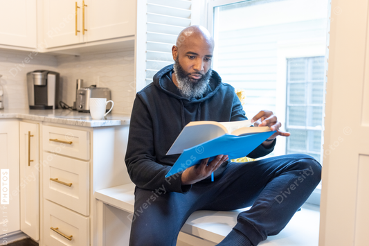 Black man, cozy, reading book in nook at home