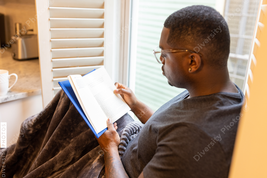 Black man, cozy, reading book in nook at home