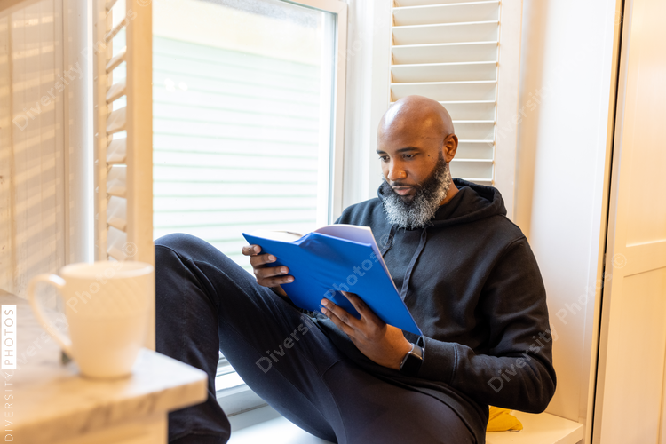 Black man enjoys reading book at home in nook, cozy and comfortable