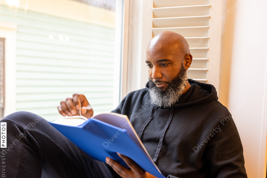 Black man enjoys reading book at home in nook, cozy and comfortable