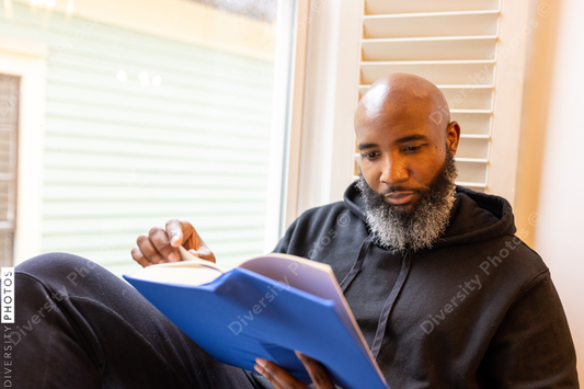 Black man enjoys reading book at home in nook, cozy and comfortable