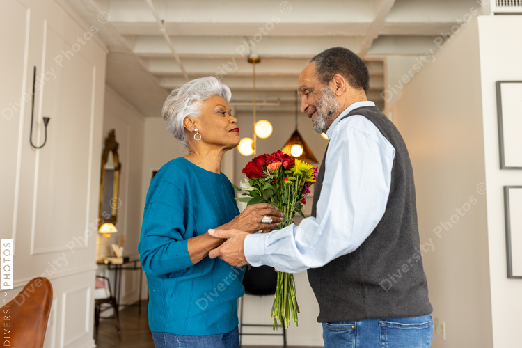 Black senior couple embracing, celebrating their love with rose flowers at home
