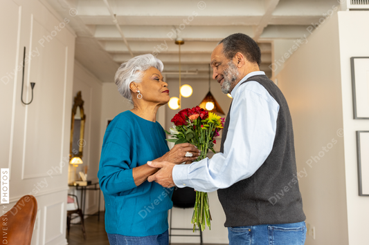 Black senior couple embracing, celebrating their love with rose flowers at home