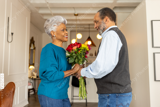 Black senior couple embracing, celebrating their love with rose flowers at home