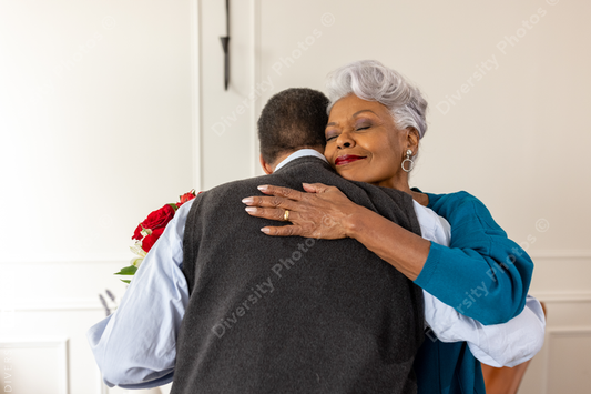 Black senior couple embracing, celebrating their love with rose flowers at home