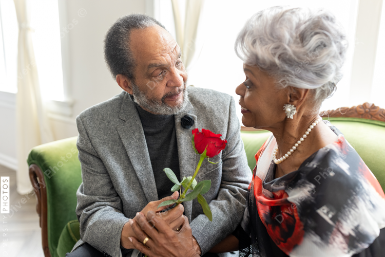 Senior African American man gives rose to wife, to commemorate thier enduring  love and anniversary