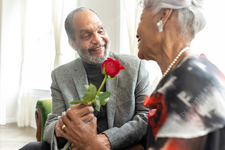 Senior African American man gives rose to wife, to commemorate thier enduring  love and anniversary