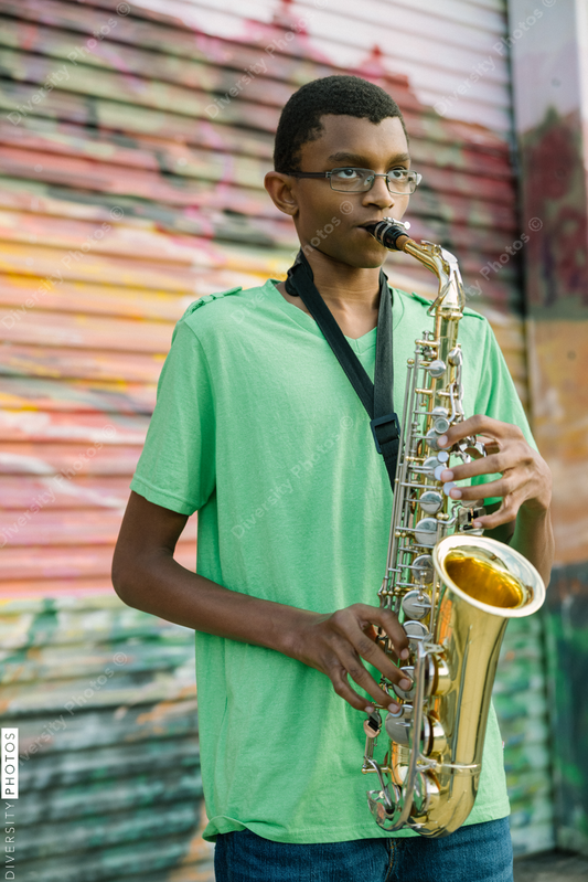 Black teen male playing saxophone at school on colorful background